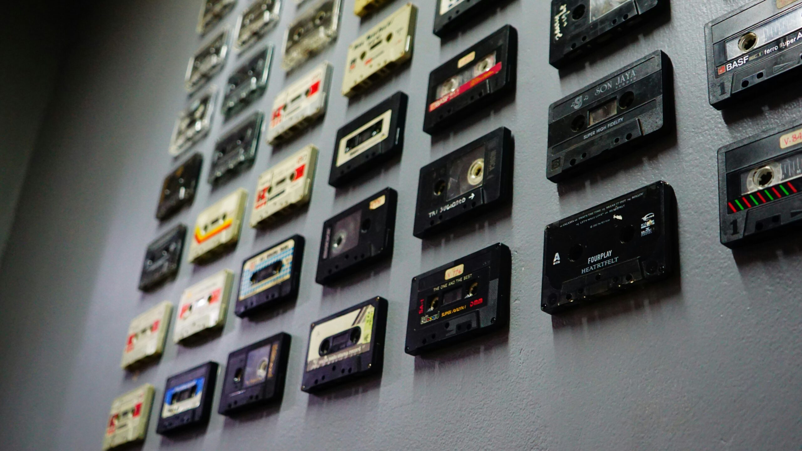 A wall decorated with rows of old audio cassette tapes in different colors and designs, organized in a grid pattern.